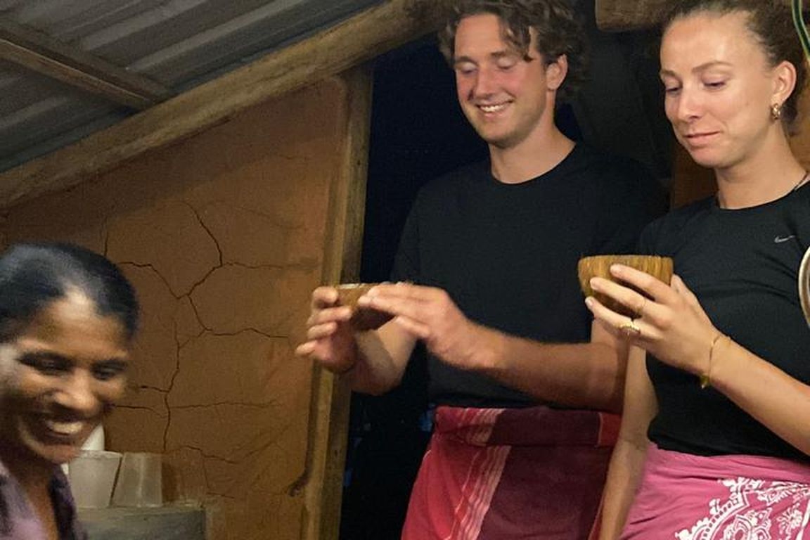 Guests with a local cook beside clay pots in a village kitchen