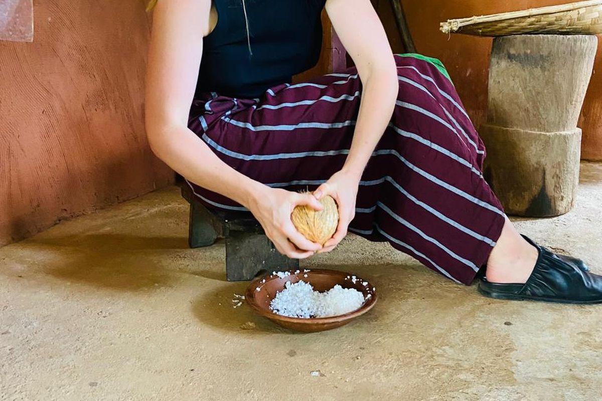 Guest scraping fresh coconut on the floor of a village kitchen