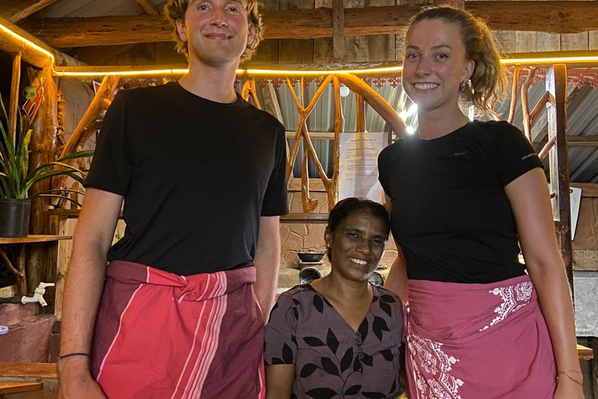 Two guests and their local host cook in aprons in a clay-walled kitchen